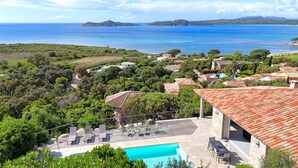 Una villa costera con piscina, mobiliario exterior y vistas al mar y las colinas.