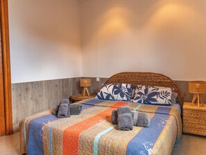 A neatly made bed with a patterned bedspread, two pillows with a floral design, and two rolled towels on the bed. - Villa Bella Vista Di Pinarello (Zonza)