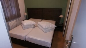 Ein Doppelbett mit weißen Leinen, ein Holz-Kopfteil, ein Nachttisch mit Lampe und ein Fenster mit Vorhängen.