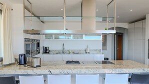 A modern kitchen with a central island, stainless steel appliances, and white bar stools. - Villa Ghjiseppina Di Pinarello (Porto-Vecchio)