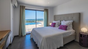 A bedroom with a large bed, a desk, and a view of a swimming pool and landscape. - Villa Ghjiseppina Di Pinarello (Porto-Vecchio)