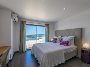 Ein Schlafzimmer mit einem großen Bett, einem Schreibtisch und Blick auf Pool und Landschaft.