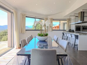 Eine moderne Küche mit einer großen Kochinsel, einem Essbereich mit Glastisch und Blick auf die Berge.