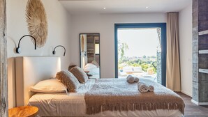 Camera da letto moderna con un letto grande, un comodino in legno e vista su una piscina e del verde all'esterno.