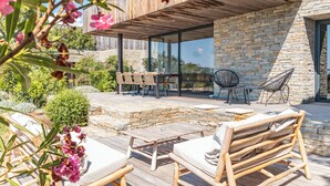 Patio moderno all'aperto con mobili in legno, pareti in pietra e zona pranzo con vetrate.