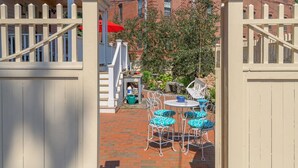 A gated patio area with a brick pathway, a small table with chairs, and a red umbrella.