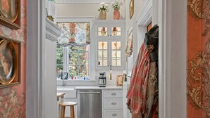 A narrow hallway leading to a kitchen with white cabinets, a stainless steel sink, and a coffee maker.