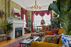 Una sala de estar tradicional con chimenea, muebles ornamentados y exuberantes plantas verdes.