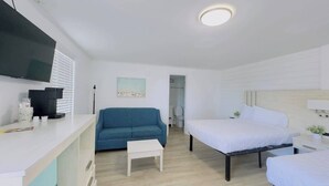 Een moderne hotelkamer met een flatscreen televisie, een blauwe bank, een wit bed en een klein witte tafeltje.