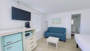 Een slaapkamer met een bed, een blauwe bank, een televisie, een koffiezetapparaat en een kleine tafel.