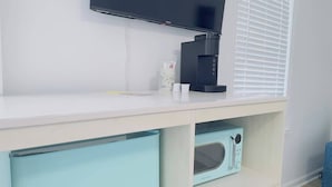 Een moderne kamer met een flatscreen televisie aan de muur, een koffiezetapparaat en een magnetron op een lichtblauwe kast.
