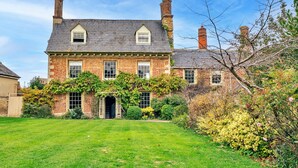 Une grande maison en briques, dotée d’une façade symétrique, de nombreuses cheminées et d’un jardin bien entretenu.