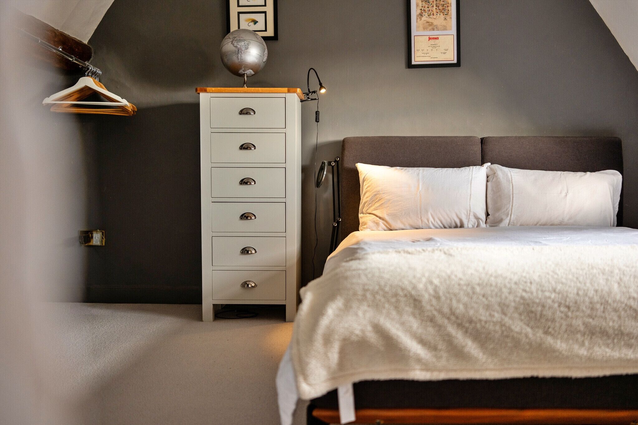Ein Schlafzimmer mit einem Bett, einem Schminktisch, einem Globus und einem gerahmten Bild an der Wand.