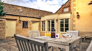 Un espace de restauration extérieur rustique, avec une table et des chaises en bois, un bâtiment en briques doté d’une fenêtre et d’une porte.