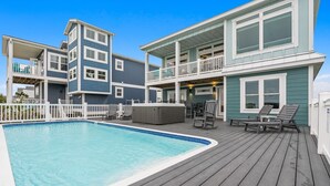 Una casa de dos pisos con piscina, sillas de deck y bañera de hidromasaje.