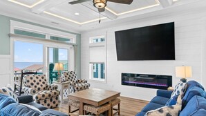 Un salón con televisor grande, chimenea y vista al océano.