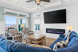 A living room with a large TV, a fireplace, and a view of the ocean. - Experience ocean views at Atlantic Horizon in Oak Island, featuring 10 bedrooms. (Oak Island)
