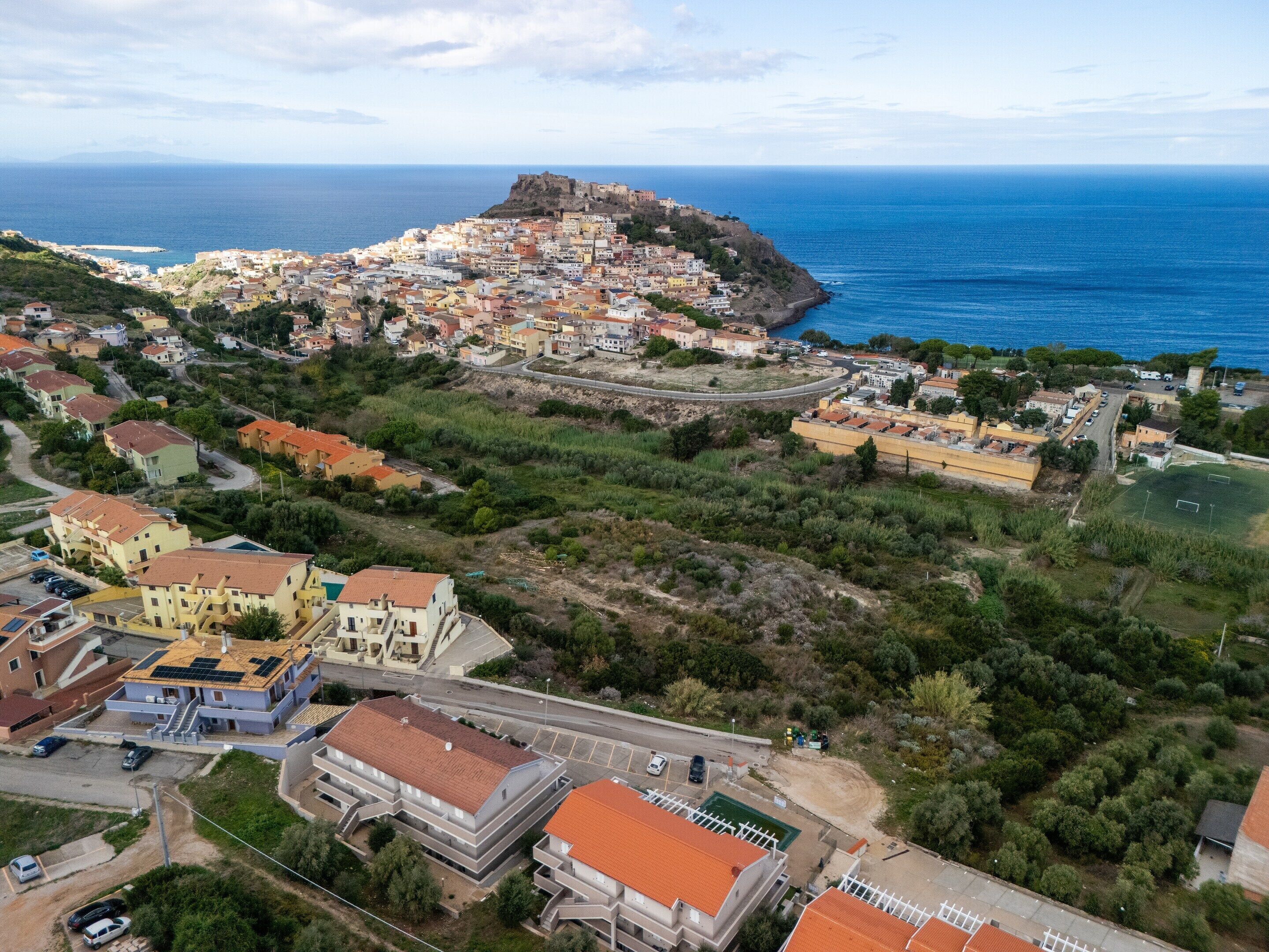 A coastal town with a prominent fort on a hill, residential buildings, and a clear view of the sea.