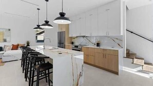 Egy modern konyha központi szigettel, fekete székekkel és mennyezetről lógó lámpákkal.