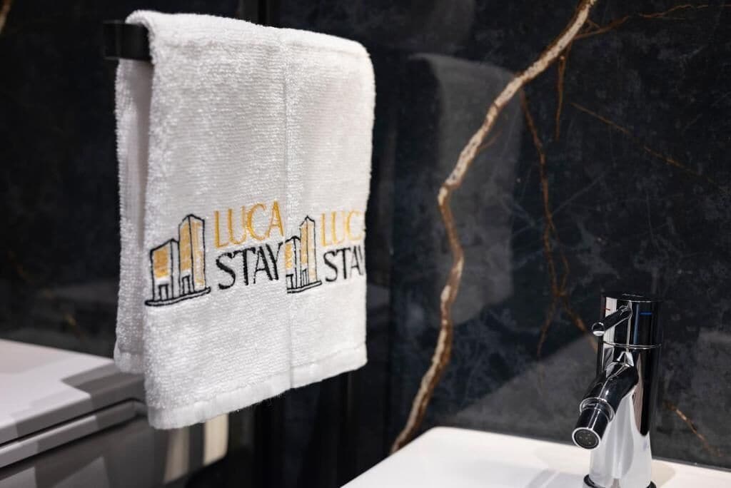Ein weißes Handtuch mit der Aufschrift "Luca Stay", das an einer schwarzen Marmorwand hängt.