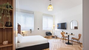 A modern hotel room with a bed, two chairs, a small table, a TV, and a mirror. - Luca Stay Duomo Visconti Suites (Milan)