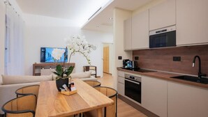 A modern kitchen with a wooden countertop, built-in oven, and a sink. There is a dining area with a wooden table and wicker chairs. A potted orchid is on the table. - Luca Stay Duomo Visconti Suites (Milan)