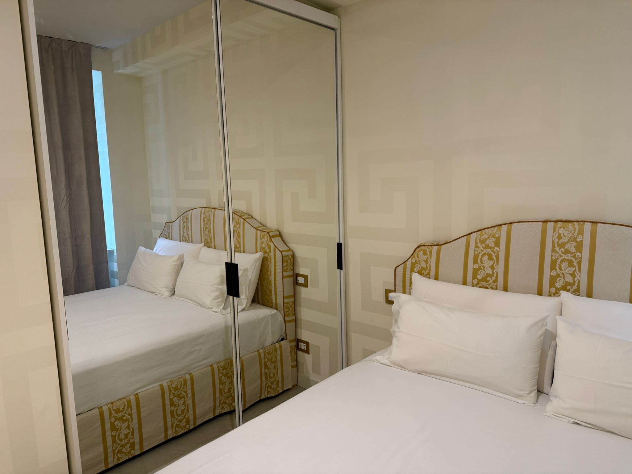 Ein Hotelzimmer mit zwei Betten, jeweils mit einem gemusterten Kopfteil und weißer Bettwäsche.