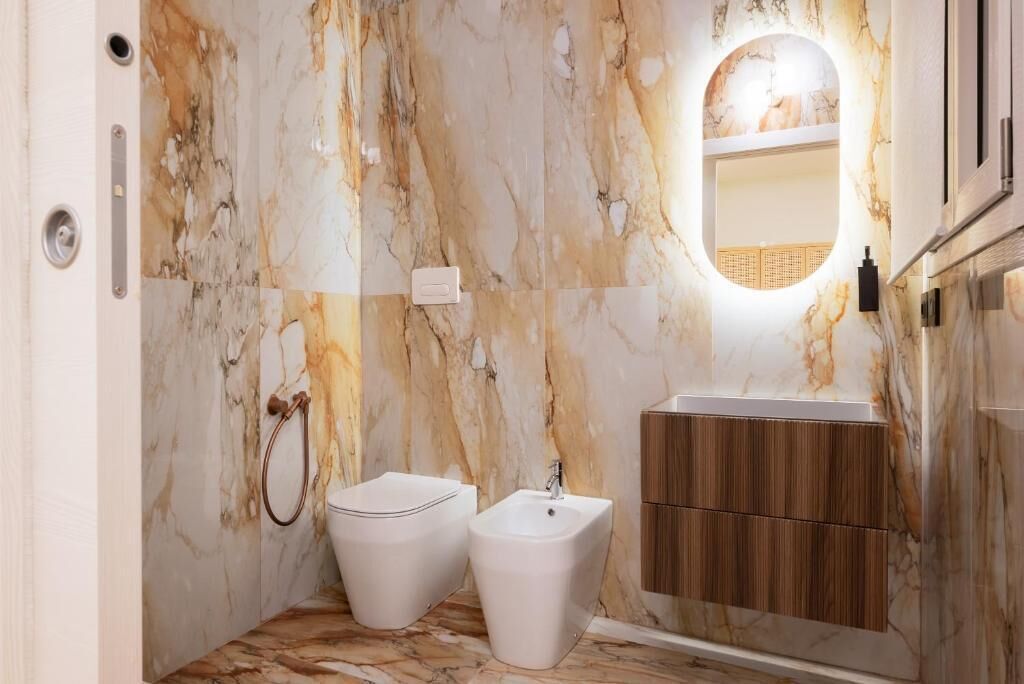 A bathroom with marble walls, a wooden vanity, and two bidets.