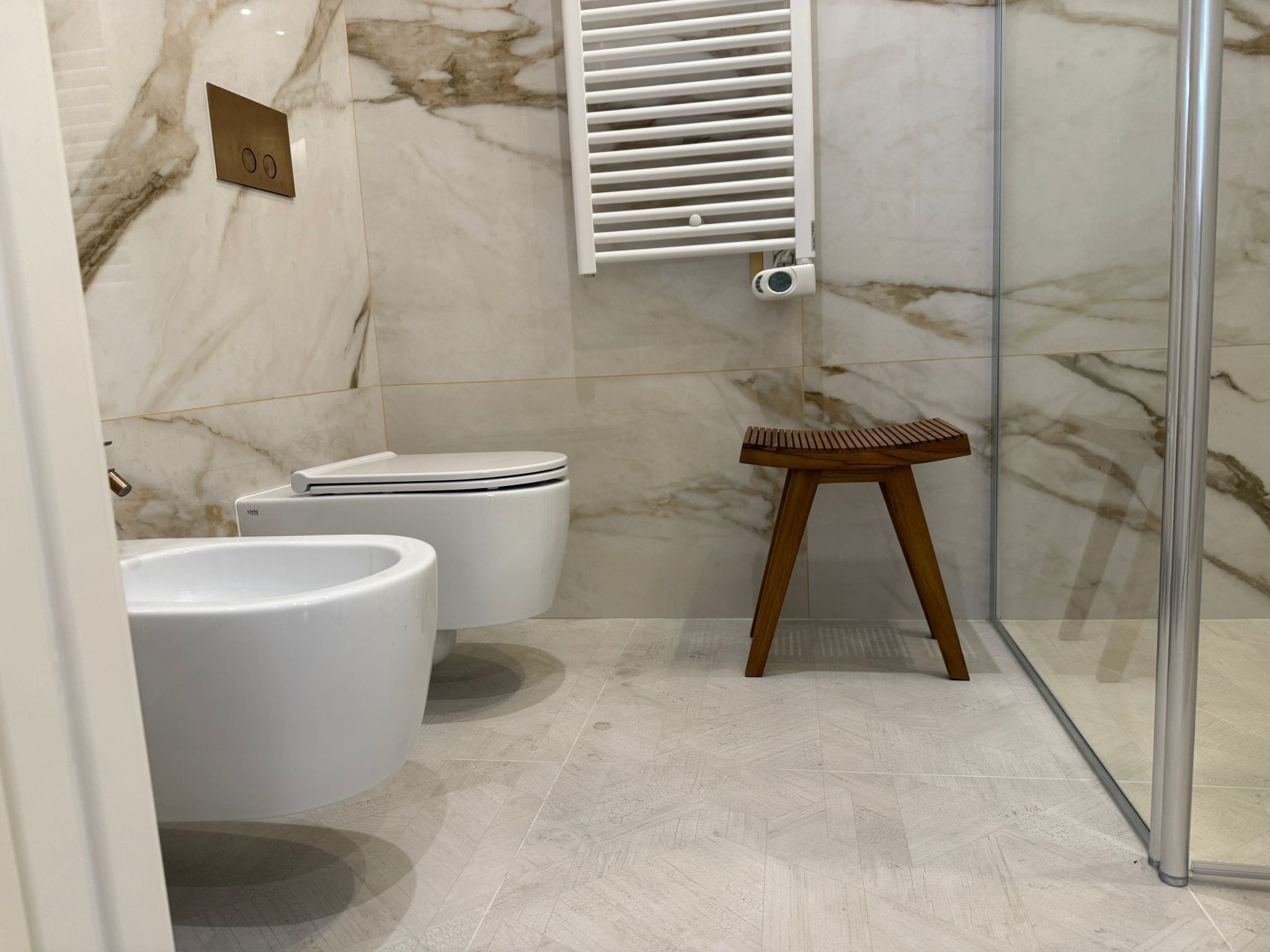 A bathroom with a toilet, bidet, and a wooden stool.