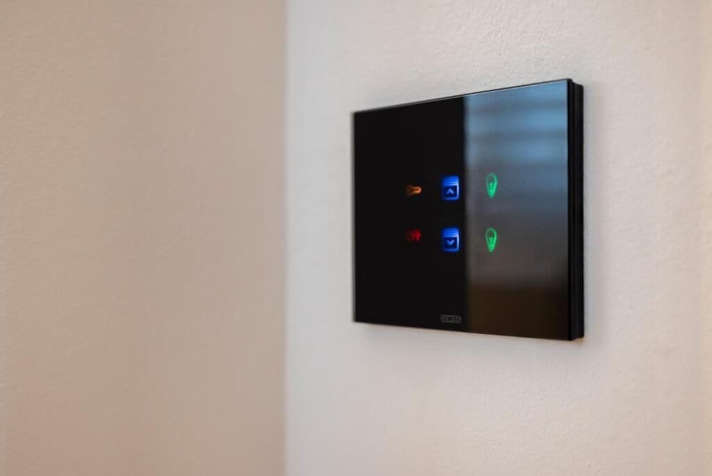 A modern, wall-mounted thermostat with four control buttons and a digital display.