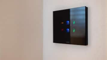 A modern, wall-mounted thermostat with four control buttons and a digital display.