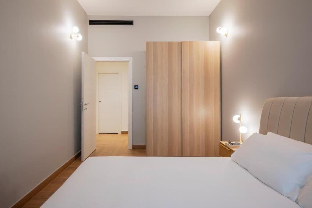 A modern hotel room with a large bed, a wooden wardrobe, and bedside lamps.