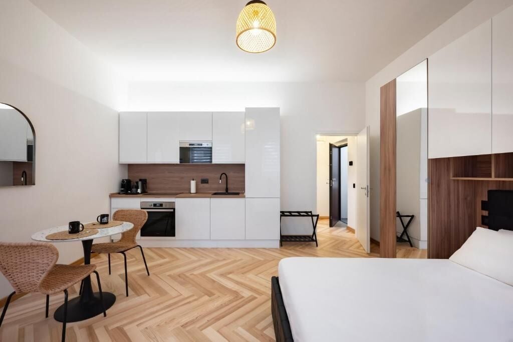 Une chambre d’hôtel compacte comprenant un coin cuisine, un espace repas avec une table ronde et des chaises, un lit et un grand miroir.