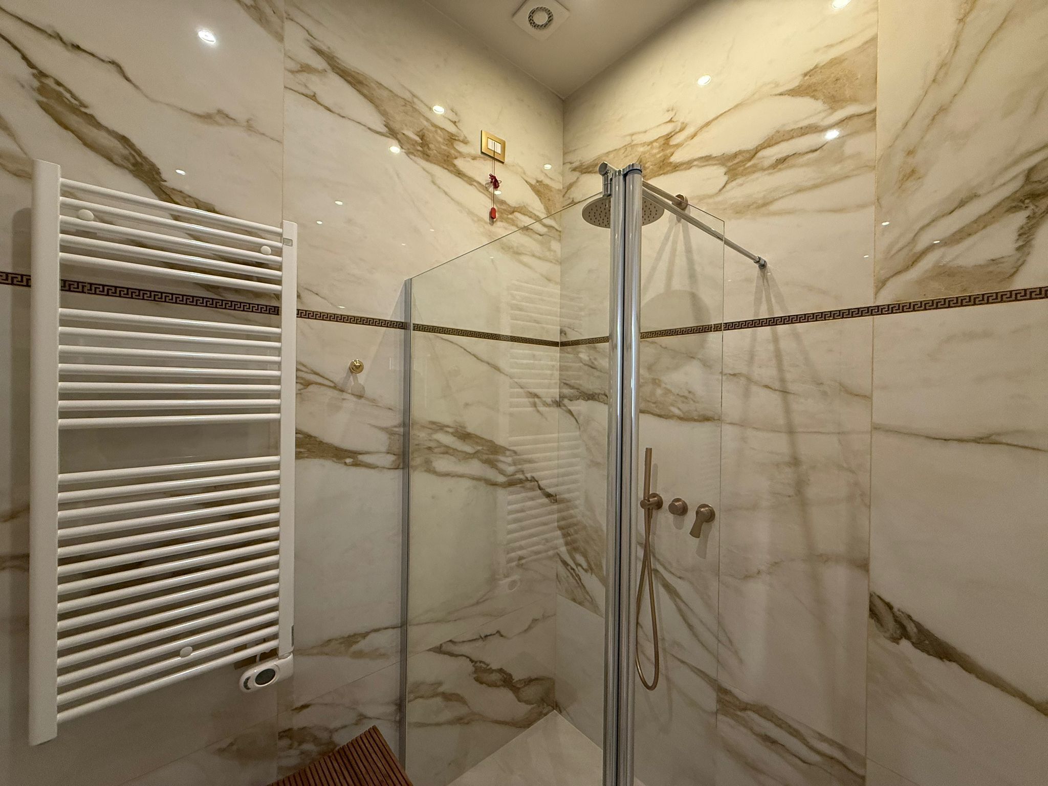 A modern bathroom with a glass-enclosed shower, marble walls, and a white towel rack with a decorative pattern.