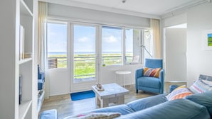 A bright living room with a large window, a blue armchair, a white coffee table, and a blue sofa. - 2 Person Apartment With sea View (De Koog)