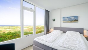 A bedroom with a large window, a bed, a chair, and a painting on the wall. - 2 Person Apartment With sea View (De Koog)