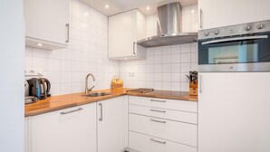 A modern kitchen with white cabinets, a wooden countertop, a stainless steel oven, and a built-in range hood. - 2 Person Apartment With sea View (De Koog)