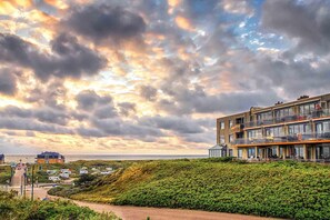 A coastal hotel with multiple balconies overlooking the sea, a paved walkway, and a landscaped area with dense greenery. - 2 Person Apartment With sea View (De Koog)