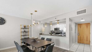 A modern dining area with a wooden table and chairs, a clock on the wall, and a kitchen in the background. - 1BR Retreat | Free Parking | Rooftop Pool (Miami)