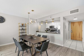 Ein zeitgemäßer Essbereich mit Holztisch und Stühlen, einer Uhr an der Wand und einer Küche im Hintergrund.