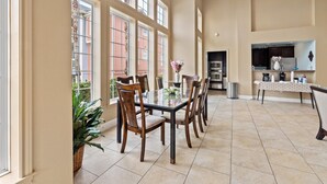 Un comedor amplio con una mesa grande y sillas, una zona de cocina con electrodomésticos modernos, y ventanas grandes que ofrecen luz natural.