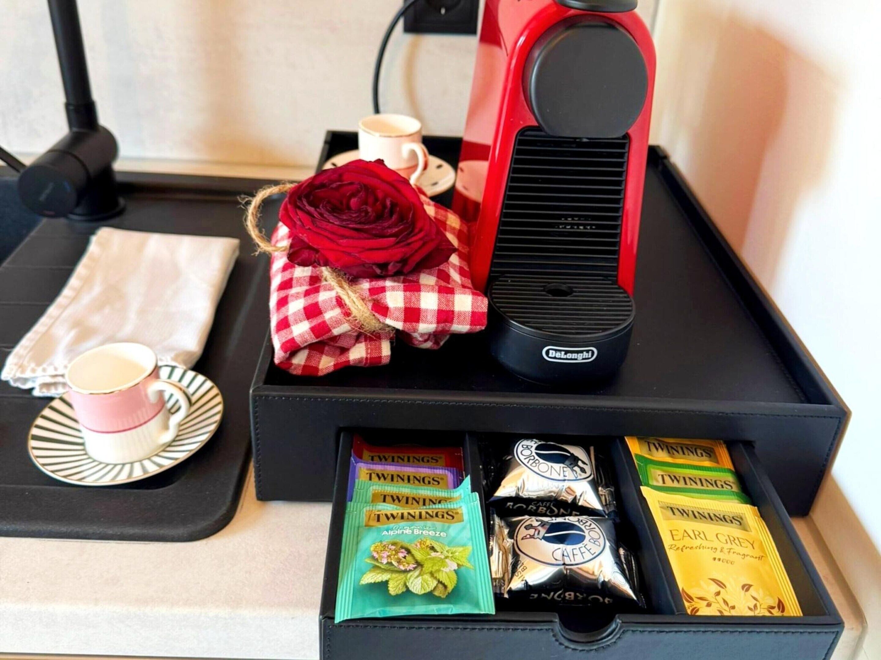 A tray with a coffee maker, a red rose, a cup of coffee, a napkin, and Twinings tea packets.