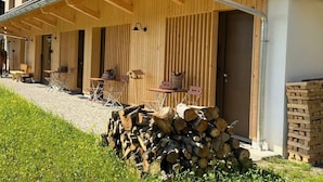 Un edificio de madera con un área de estar al aire libre cubierta, un letrero que dice 'Sausteig 133a' y pilas de leña.