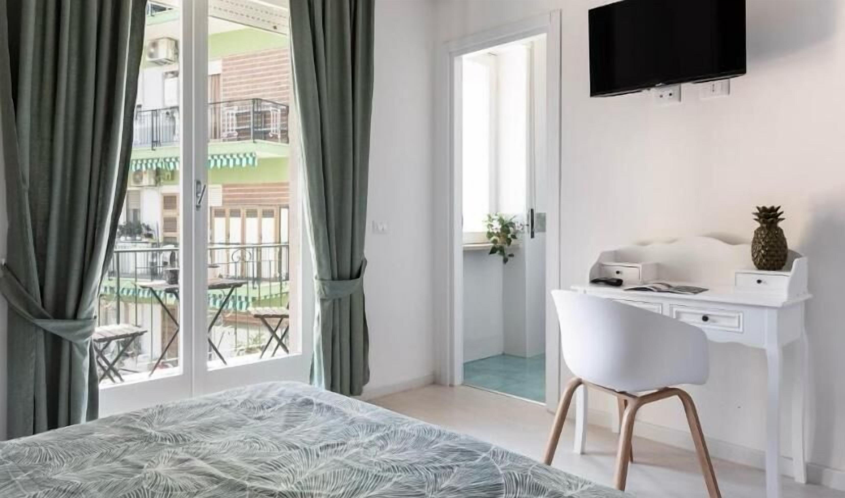 Une chambre d’hôtel comprenant un lit, un bureau, une chaise, une télévision et un balcon avec vue sur l’extérieur.