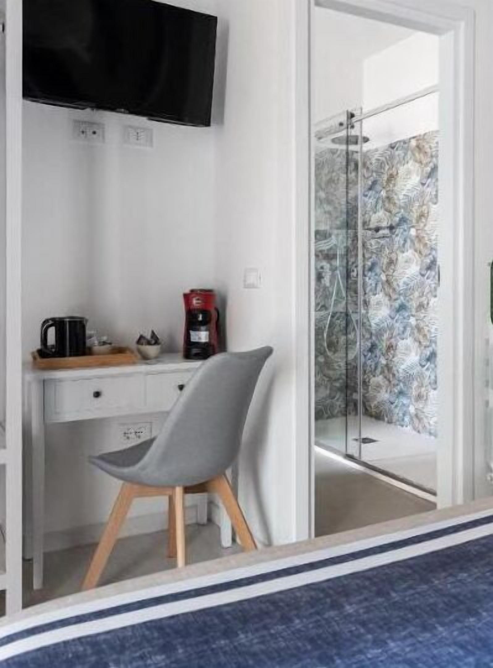 A modern room with a desk, chair, coffee maker, and a TV mounted on the wall.