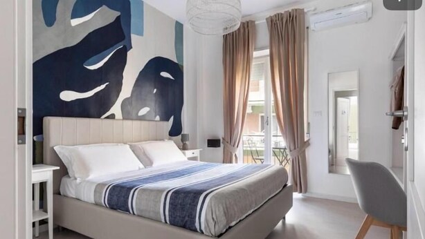 A modern bedroom with a large bed, a side table, a chair, and a view of the outdoors.