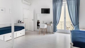 A bedroom with a bed, a desk, a chair, a TV, and a balcony with curtains.