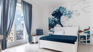 A bedroom with a white bed, a large wall mural, and a view of the outside balcony.