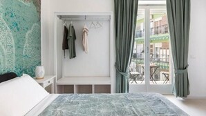 A bedroom with a bed, a wardrobe, and a balcony with a view.
