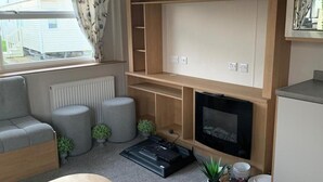 Ett kompakt vardagsrum med en soffa, två sittpallar, en liten TV och en liten köksdel.